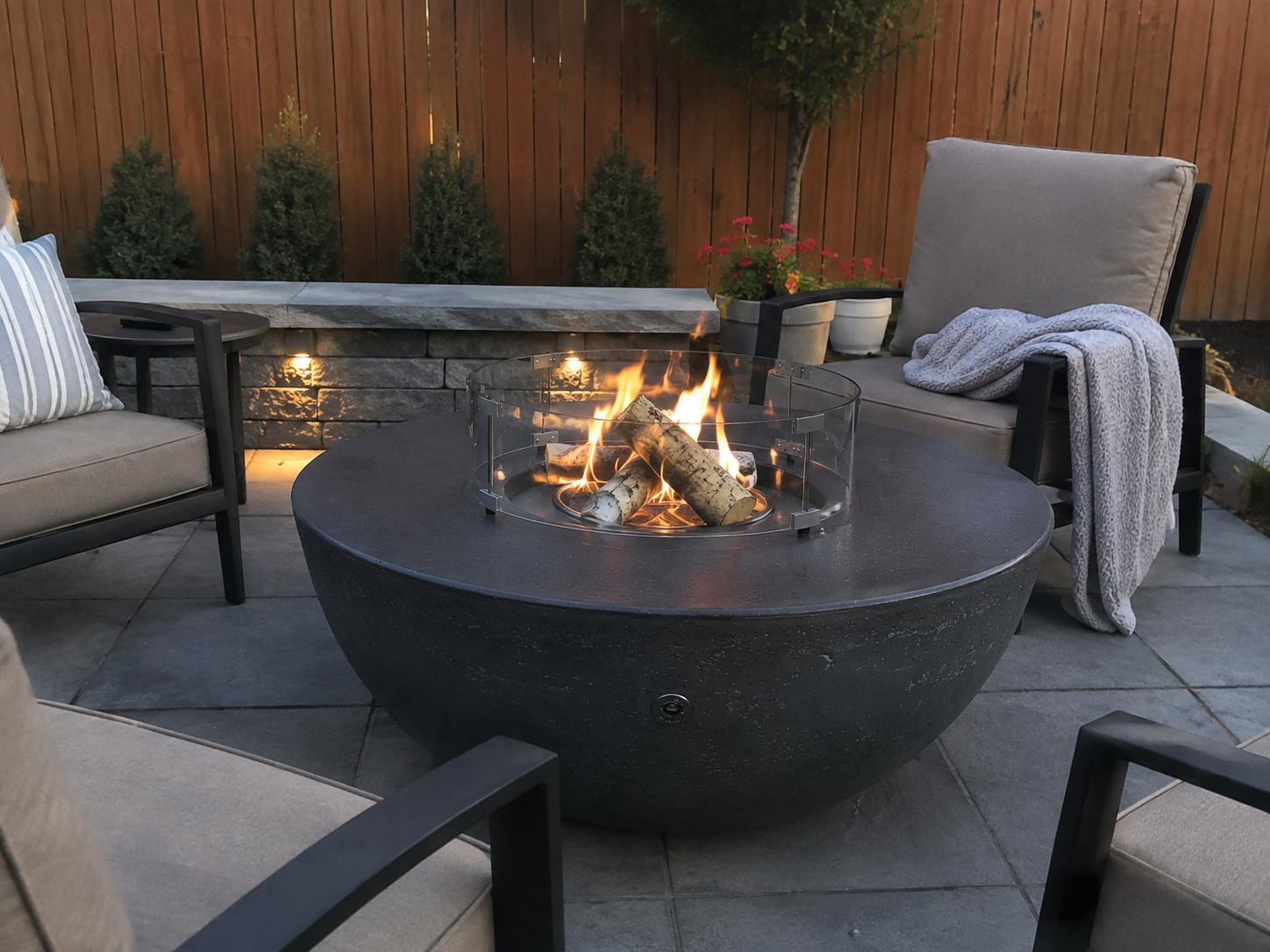 White sculptural round concrete fire table surrounded by Adirondack chairs and deep seating sofa — modern outdoor living